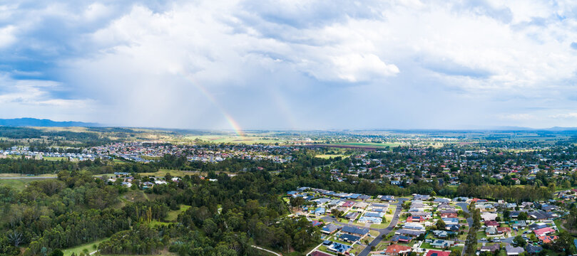 Aerial view over residential area of town, rainfall and rainbow over distant farms