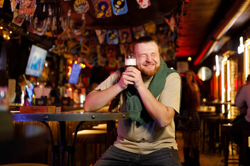 Obraz premium Relaxing after hard working day. happy young men holding glass with beer and smiling while sitting at the bar counter