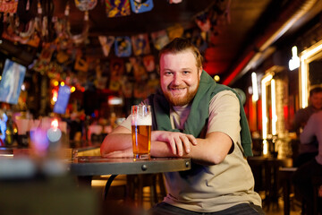 portrait of a cheerful red-haired guy with a beer at a table in a pub