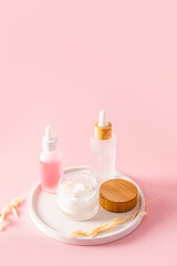 A moisturizing cosmetic product in white matte bottles on a white plaster tray and a pink background. Vertical view. A copy space.