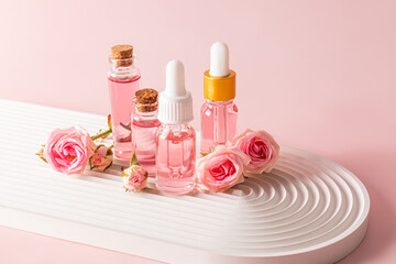 A set of cosmetics based on rose oil, bottled rose water with a lid stand on a white podium, a...