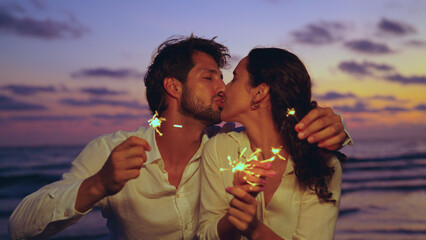 Young latin couple playing sparklers on beach at sunset. They having fun dancing enjoying holiday on the beach.