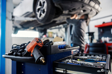 Selective focus on a drill and drawer with tools on a mechanic toolbox with worker fixing car in...