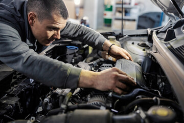 Fototapeta na wymiar A mechanic is putting on car battery under the hood in mechanic's shop.
