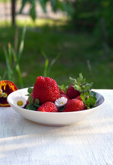 Fresh berries red strawberry with flowers daise and pansy, green leaves on a white wooden table on green natural blur background