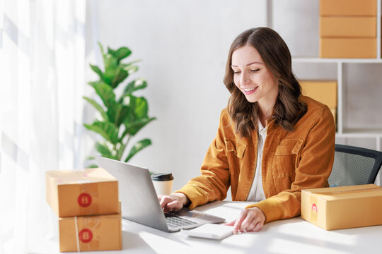 Concept of parcel delivery and selling online, Female seller or retailer using laptop to check sales of the day on online store to be packed into the parcel and ready to deliver to the customer