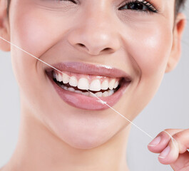 Make sure to floss. Studio portrait of an attractive young woman flossing her teeth against a grey background.