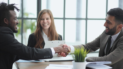 Business people shaking hands while sitting at the desk in office