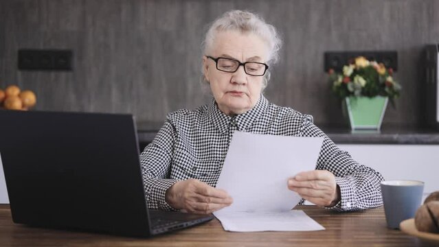 An elderly woman, a pensioner of eighty years, works with documents at a computer. Modern Grandmother