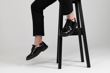 Hanging down legs of a stylish man in a sharp black formal suit sitting on a tall chair. Isolated on white background.