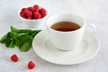 herbal tea in white cup on saucer with mint leaves and raspberry in bowl 