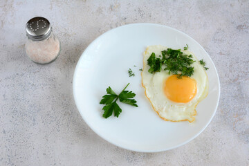 A white plate of food with a fried egg and chopped parsley on marble background