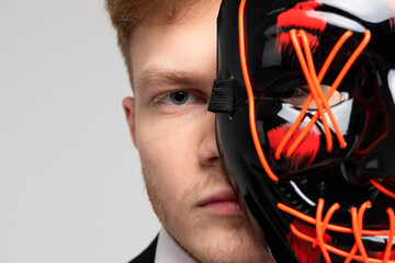 Stylish man in a sharp black formal suit covering half of his face with a bright mask. Concealed...