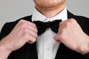 Stylish young man in a sharp black formal suit is tightening the bow, closeup, isolated on white background.