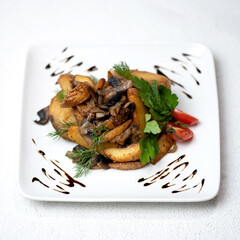 Fried potatoes with mushrooms and onions. Dish on white square plate with tomato and parsley. Vegetarian dish. Lunch at home. White background. Soft focus. View from above. Copy space.