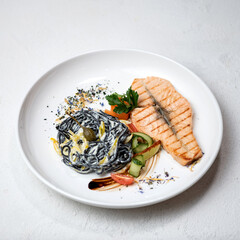 Salmon steak with vegetables and noodles on white plate. Pasta with salmon. Complex lunch. View from above. White background. 