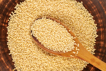 Millet from a wooden spoon on a clay dish, macro, top view.