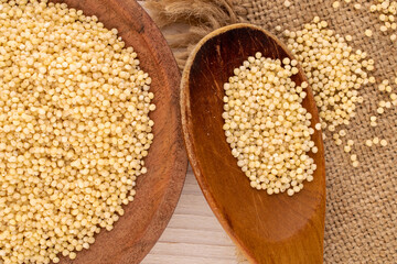 Millet in wooden cup with wooden spoon and jute napkin on wooden table, macro, top view.