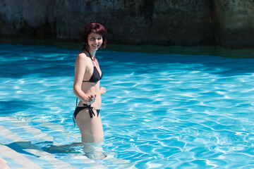 Obraz premium A woman in a bikini enters the cold water of the pool. Off season at the hotel.