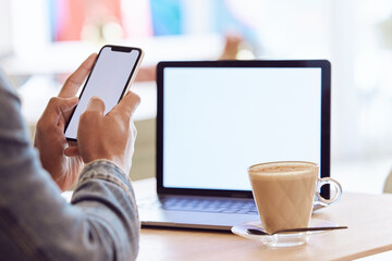 What a great work space. a man using his smartphone and laptop to work in a coffee shop while enjoying a cup of coffee.