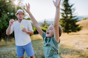 Young father and his little daughter having fun while blowing soap bubbles on a summer day in nature.
