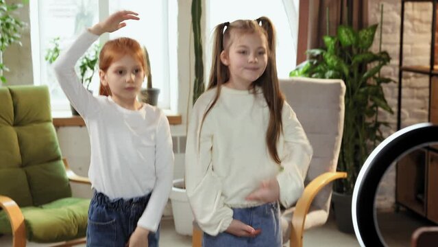 Beautiful little girls, children in casual clothes dancing modern trends in social media, recording video with mobile phone at home. Mass media, blogging, modern technologies, childhood, fun concept