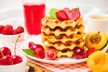 Stack of belgian waffles with fresh strawberries, cherry and apricot on white plate