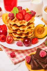 Healthy Breakfast set with Belgian waffles with strawberries, apricots, cherries, juice and a cup of black coffee and bitter chocolate on white stone table background