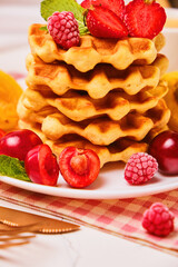 Stack of belgian waffles with fresh strawberries, cherry and apricot on white plate