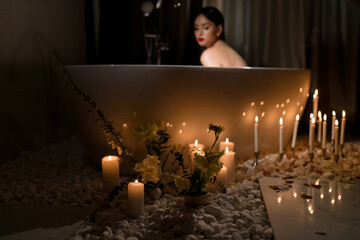 Romantic decor of flowers and burning candles near the bathtub with white roses and a girl