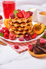 Healthy Breakfast set with Belgian waffles with strawberries, apricots, cherries, juice and a cup of black coffee and bitter chocolate on white stone table background