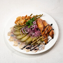 Herring with vegetables on white plate. Baked potatoes, pickled cucumbers, mushrooms, onions. Snack, pickles. White background. View from above. Copy space.