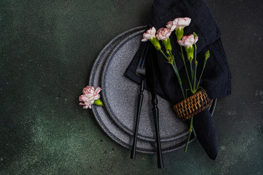 Place setting with black crockery and pink carnation flowers