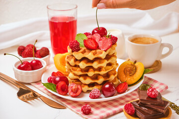 Healthy Breakfast set with Belgian waffles with strawberries, apricots, cherries, juice and a cup of black coffee and bitter chocolate on white stone table background