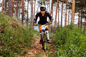 male racer athlete riding downhill race in pine forest, on him protection jacket, and knee, shin...