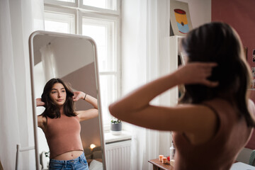 Young teenage girl looking in the mirror in her room. - obrazy, fototapety, plakaty