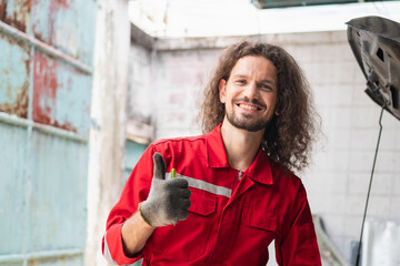 Portrait of a young car mechanic showing thumbs up in repair garage, Car repair and maintenance concepts