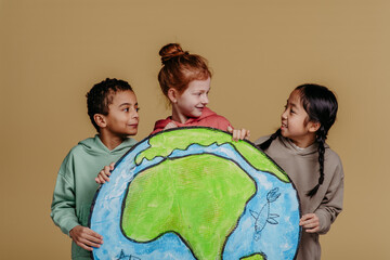 Portrait of three children with model of Earth, studio shoot. Concept of diversity in friendship.