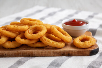 Homemade Crispy Deep-Fried Onion Rings with Ketchup on a rustic wooden board, low angle view. Close-up.