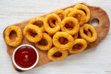 Homemade Crispy Deep-Fried Onion Rings with Ketchup on a rustic wooden board, top view. Flat lay.