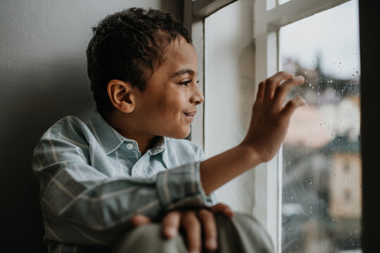 Little Multiracial Boy Looking Out Of Window.