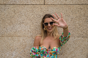Young beautiful blonde woman with sunglasses leaning against a brown wall in different postures and...