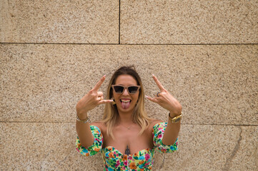 Young beautiful blonde woman with sunglasses leaning against a brown wall in different postures and...