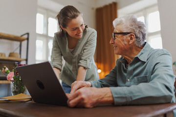 Granddaughter showing something to her grandfather on laptop.