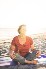 Fototapeta na wymiar Senior woman doing exercise on yoga mat at the beach, eyes closed