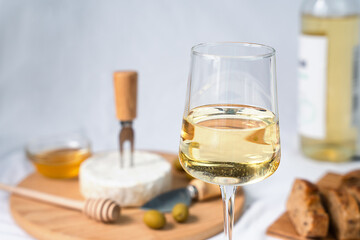A wineglass of white wine and in the background blur camembert cheese, baguette, olives and honey...