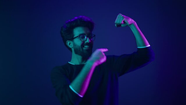 Funny Indian man slim guy fooling around show hands muscle biceps sport strong power bodybuilder ultraviolet neon studio background proud champion boast efficient security coding achievement level up