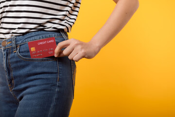 hand of person woman holding plastic credit card out of the pocket blue jean plants isolated on yellow studio background. online shopping payment, bill, currency, pay money, finance concept.