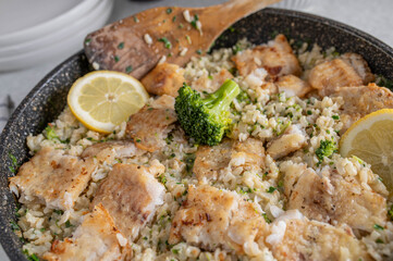 Pan fried fish fillet with brown rice, broccoli and chives in a frying pan on kitchen table