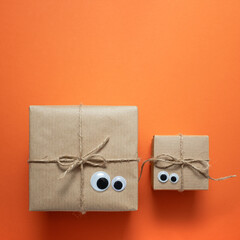 Card with brown craft gift boxes with eyes on orange background. Space for your text, square.